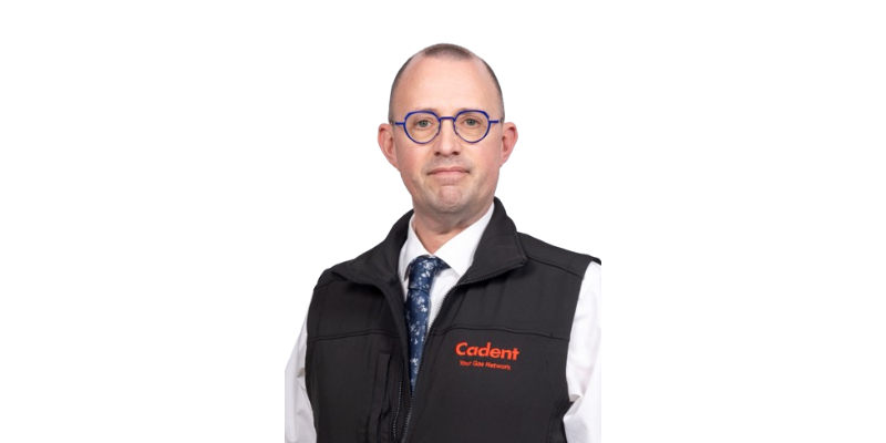 Dave Garner Photo A person wearing a black Cadent vest with a white shirt and patterned blue tie stands against a plain white background, conveying a professional demeanor.