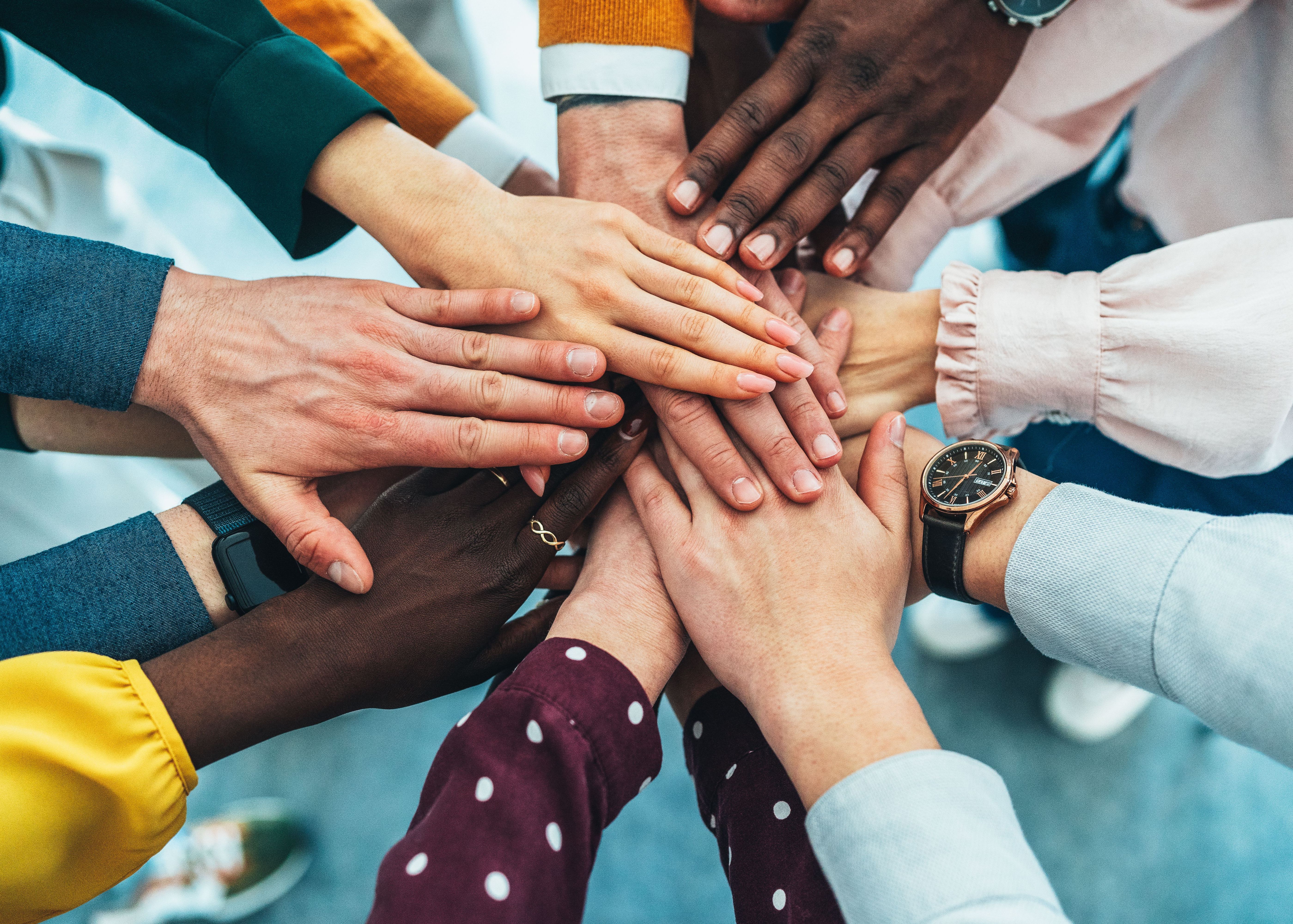 A close-up of multiple hands stacked together in a gesture of unity and collaboration. The image symbolizes teamwork, diversity, and shared goals within a professional group.
