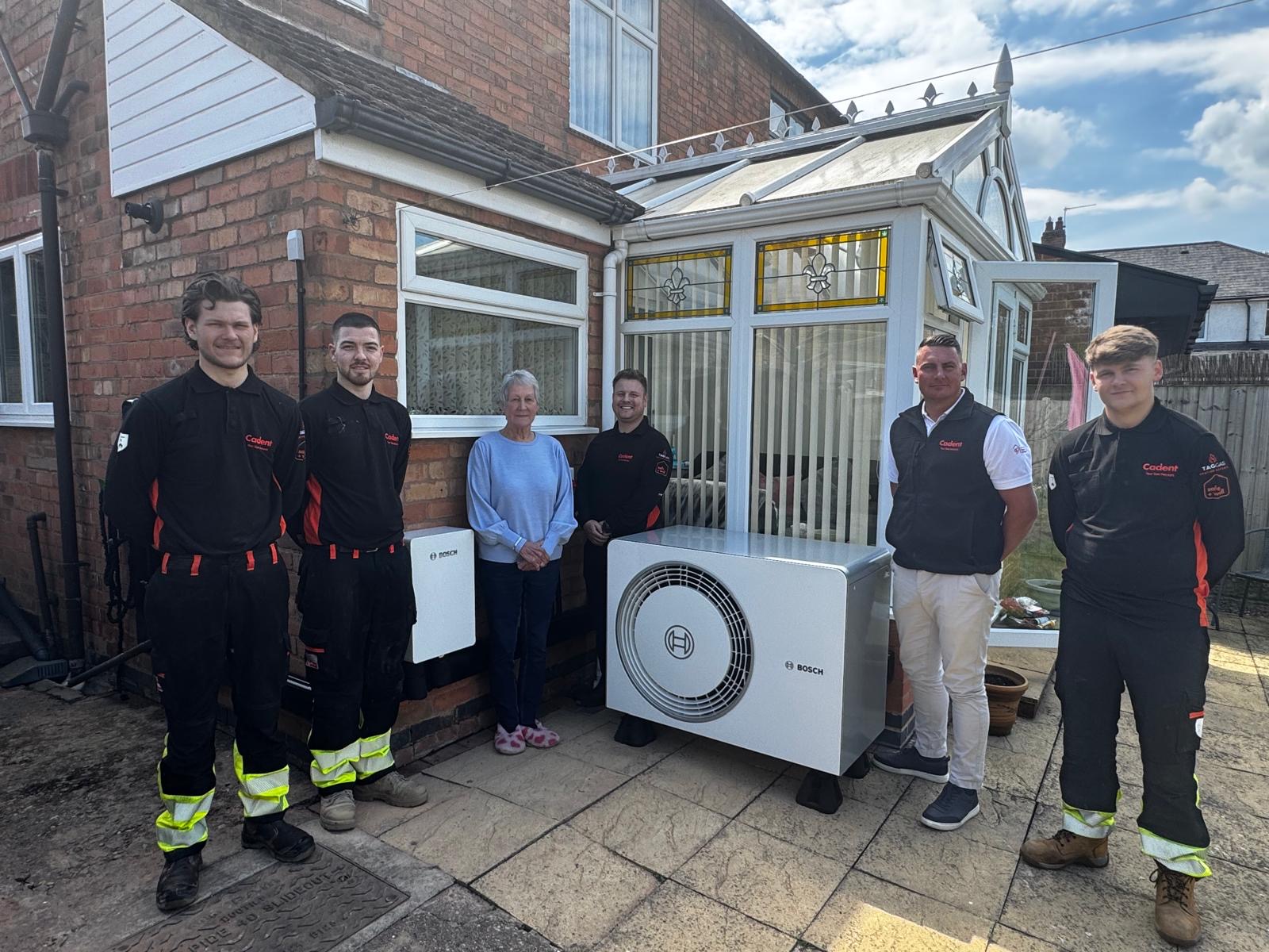 A group of five people stand smiling next to a residential building. They are posing beside a Bosch air conditioning unit on a sunny day.