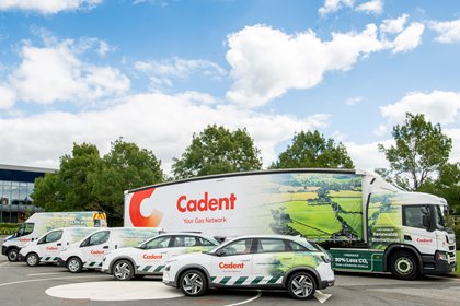 Fleet of Cadent vehicles, including trucks and cars, parked in a lot. Vehicles display landscape graphics and branding under a cloudy sky.