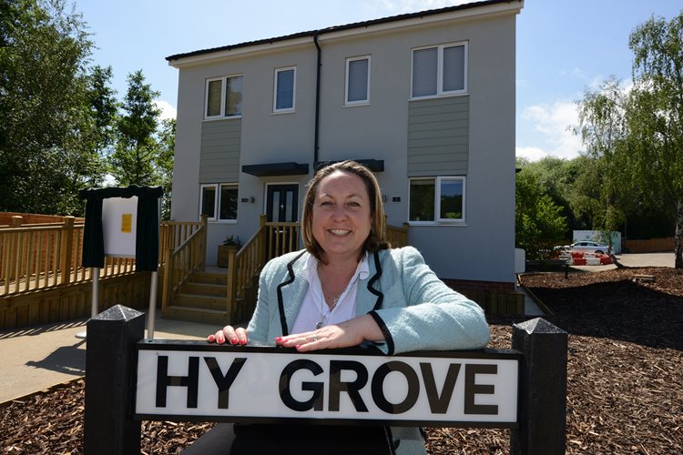 A woman in a light blue blazer smiles, leaning on a 