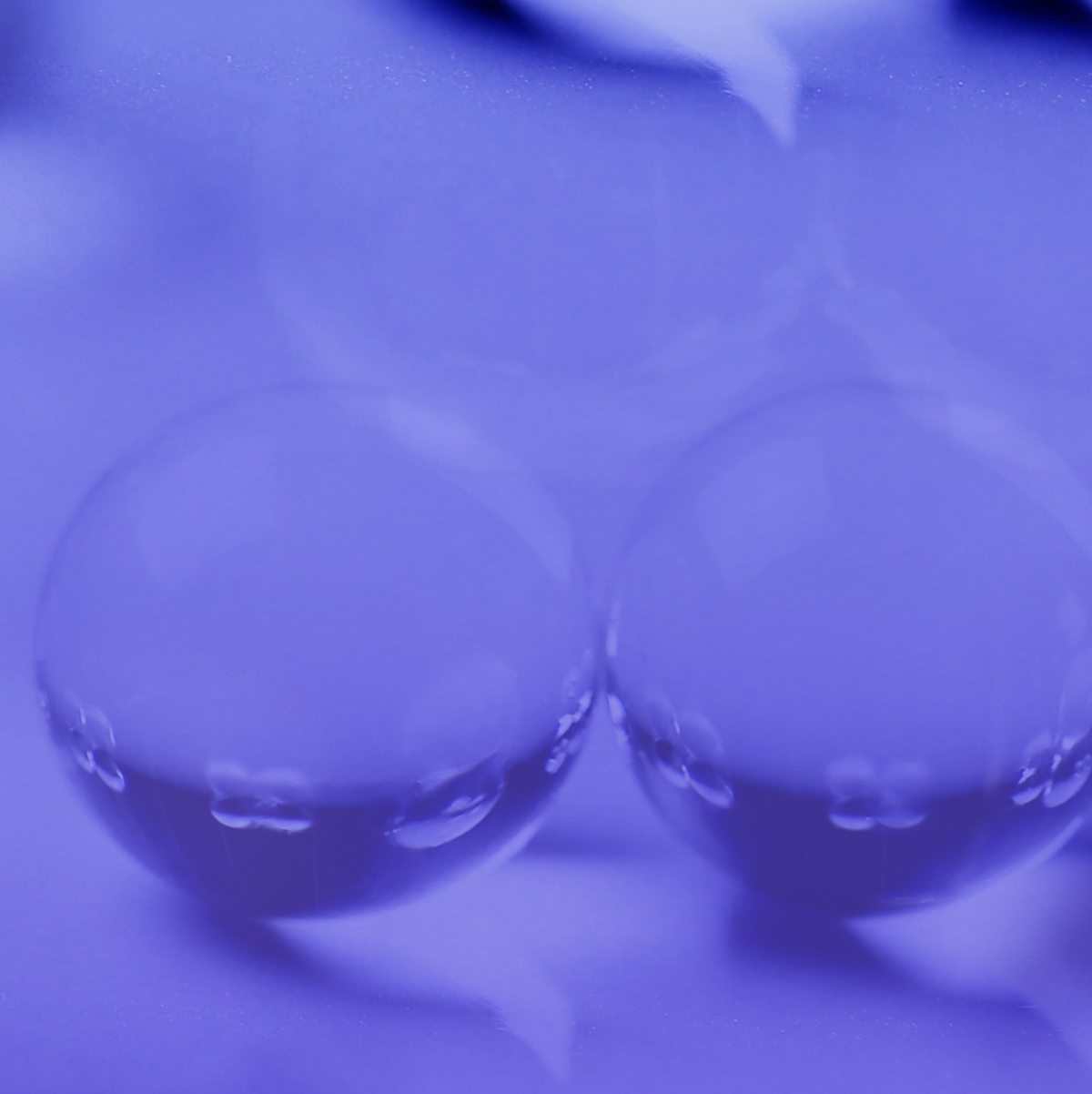 Two clear bubbles on a purple surface, reflecting light with soft highlights. The tone is serene and abstract, emphasizing simplicity and calmness.