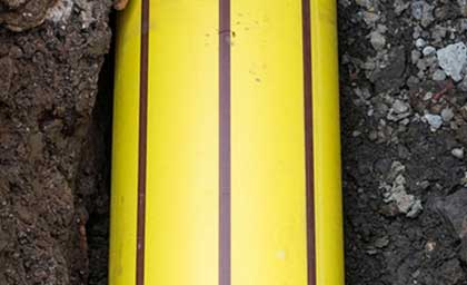 A bright yellow utility pipe with dark vertical stripes is embedded in dark soil. The image conveys a sense of industrial functionality.