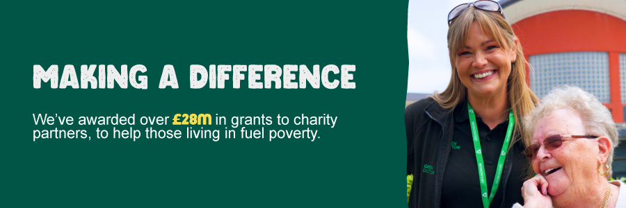 A smiling woman stands beside an older woman in a garden. The older woman, seated and wearing sunglasses, appears to be laughing, conveying a joyful atmosphere.