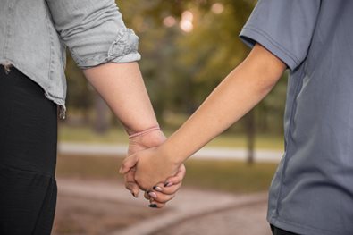 Two people holding hands outdoors, one in a denim jacket and the other in a gray shirt, convey a sense of connection and warmth in a park setting.