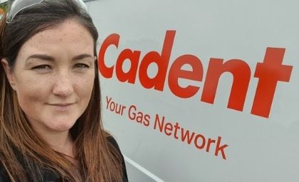 A woman with long brown hair stands in front of a van with the Cadent logo and 