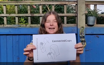 Person holding a paper with a simple line drawing of two people using cups connected by a string, labeled ‘ConnectedCups'.