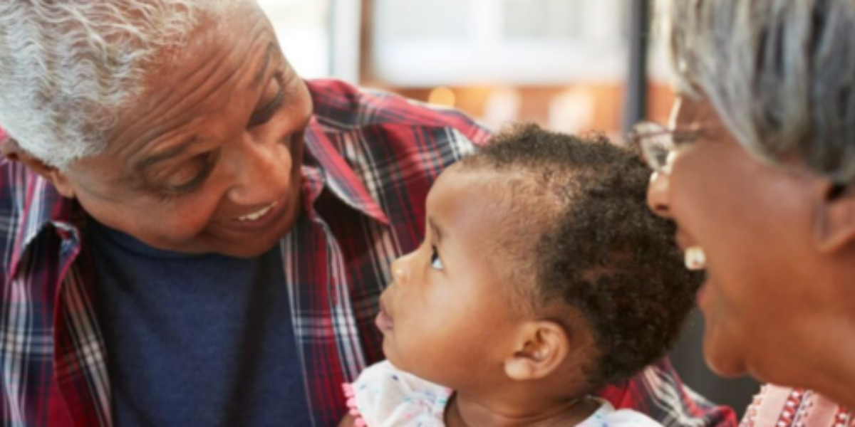 Smiling grandparents lovingly looking at their young grandchild, who is gazing back at them.