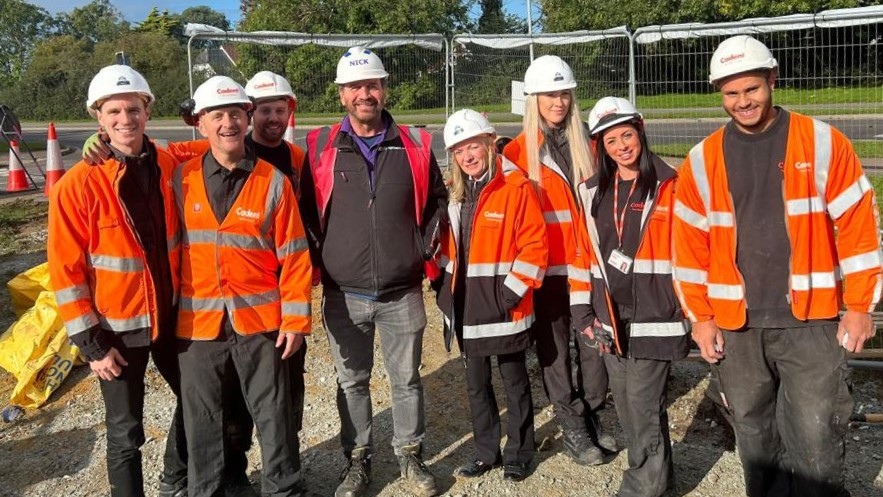 Group of workers in orange safety jackets and white helmets at a construction site