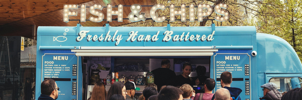 Blue fish and chips van with menu and people queuing to order food